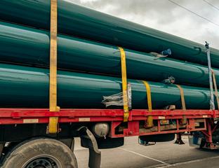 Short range photograph of a truck transporting large green pipes.
